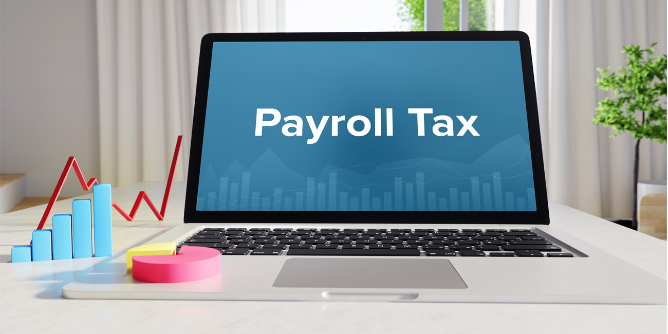 Open laptop on a desk with the words “Payroll Tax” written on the screen, while a 3-D pie graph, line chart, and bar chart are showing payroll data.